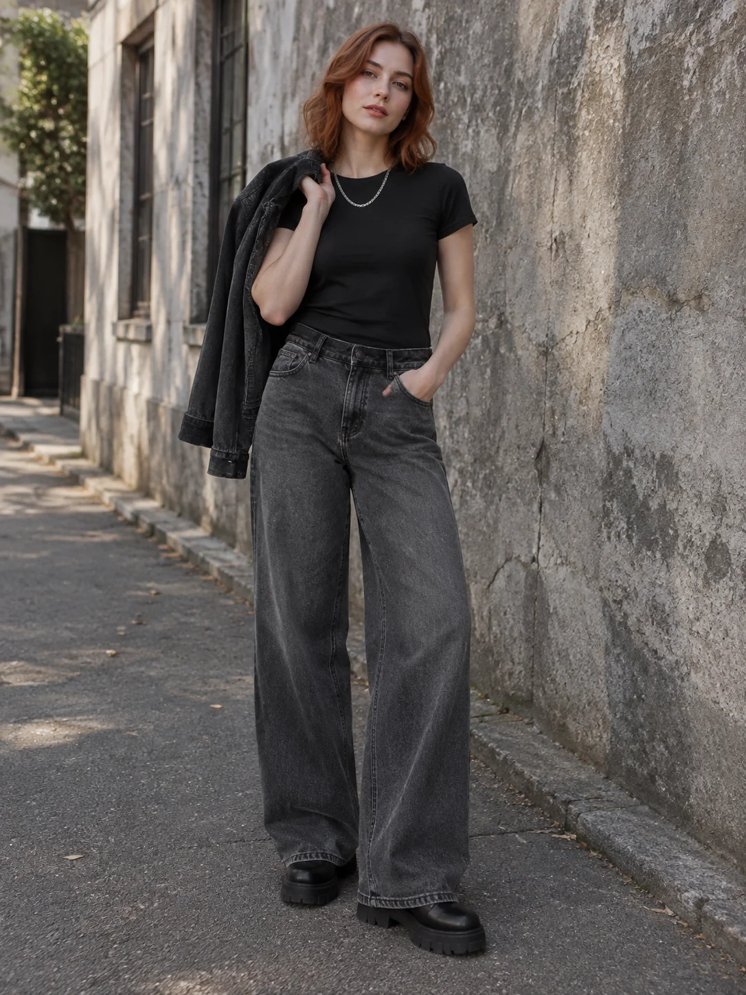 Model in grey wide-leg jeans standing against a concrete wall